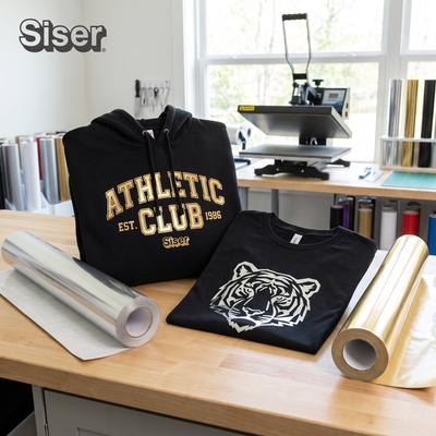 Rouleaux déroulés de flex métallisé or et argent Siser P.S. Metallic devant un t-shirt tigre et un hoodie Athletic Club
