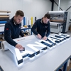 Poseurs Antalis marouflant le film translucide 3M Envision 3735 sur la face plexiglas d'une enseigne en relief